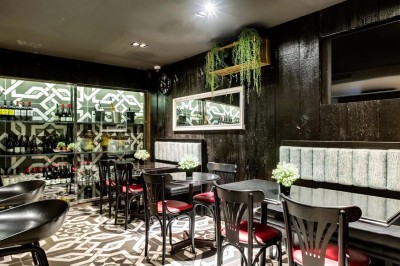 Salle de restaurant avec tables alignées, chaises noires, bouteilles de vin, plantes décoratives et murs en bois.
