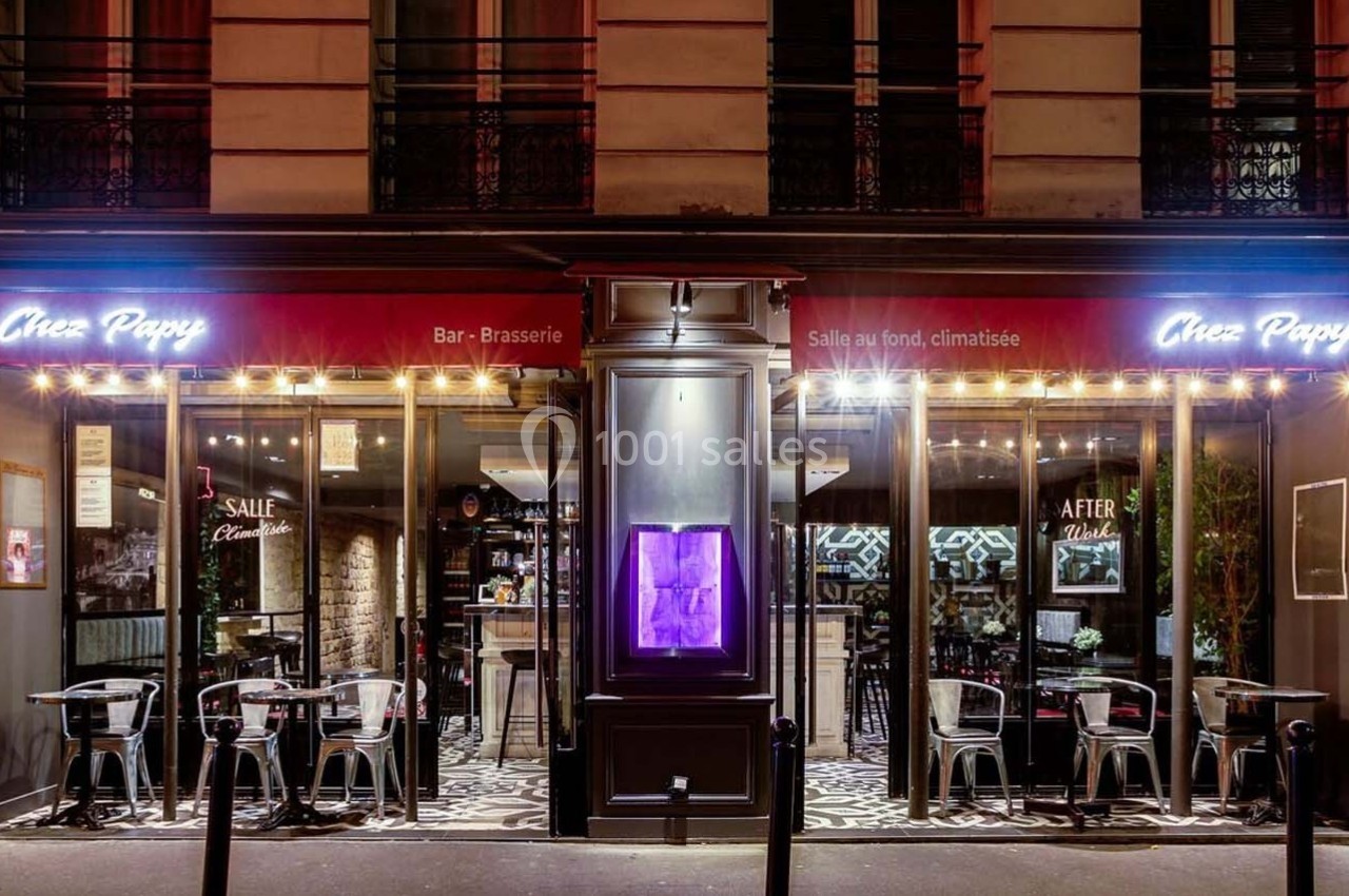 Façade d'un bar-brasserie avec terrasse extérieure, éclairage chaleureux et enseigne lumineuse ’Chez Papy’.