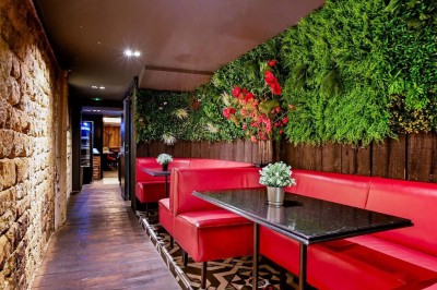 Salle de restaurant avec tables alignées, chaises noires, bouteilles de vin, plantes décoratives et murs en bois.