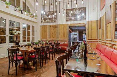 Salle de restaurant avec tables alignées, chaises noires, bouteilles de vin, plantes décoratives et murs en bois.