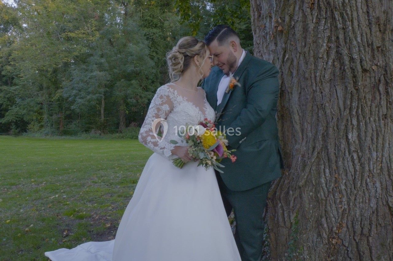 Un couple de mariés pose tendrement près d'un arbre dans un parc verdoyant.
