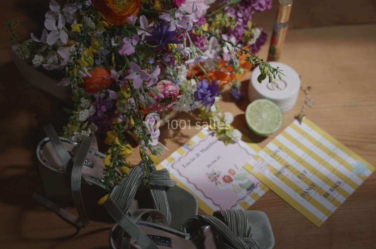 Bouquet de fleurs colorées, sandales vertes, lime coupée, bougie et carton imprimé sur une table en bois.