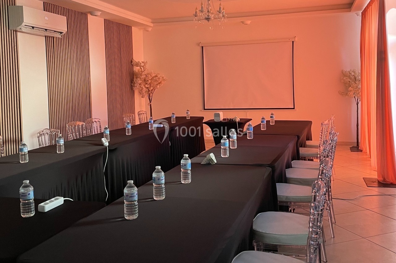 Salle de réunion avec tables noires disposées en U, chaises transparentes et écran de projection en fond.