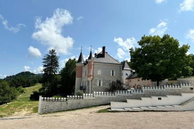 Façade d'un bâtiment en pierre avec une tour, des fenêtres blanches, une terrasse aménagée et un drapeau bleu.
