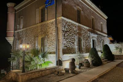 Façade d'un bâtiment en pierre avec une tour, des fenêtres blanches, une terrasse aménagée et un drapeau bleu.