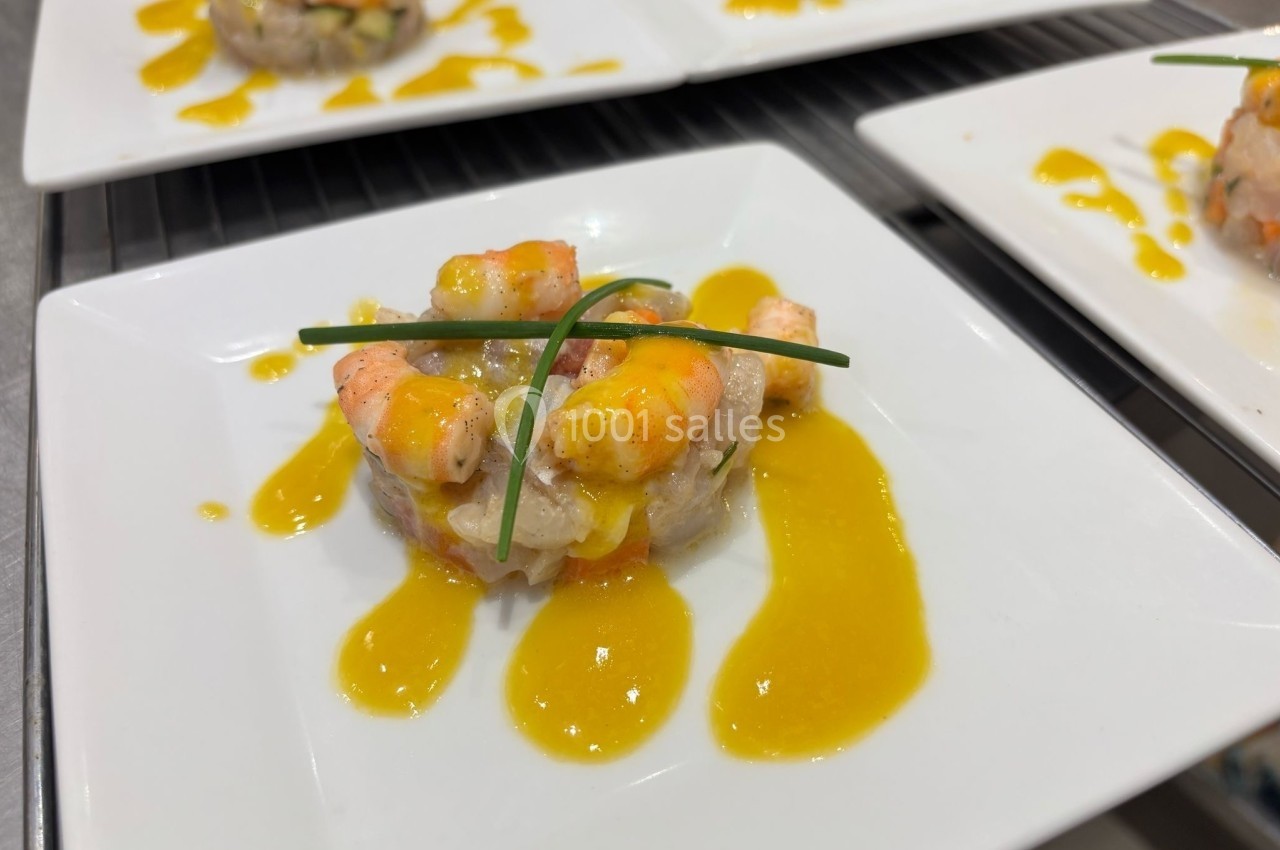 Tartare de poisson et crevettes décoré de ciboulette, nappé de sauce jaune, servi sur une assiette blanche.