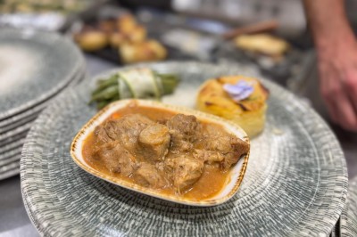 Façade d'un bâtiment en pierre avec une tour, des fenêtres blanches, une terrasse aménagée et un drapeau bleu.