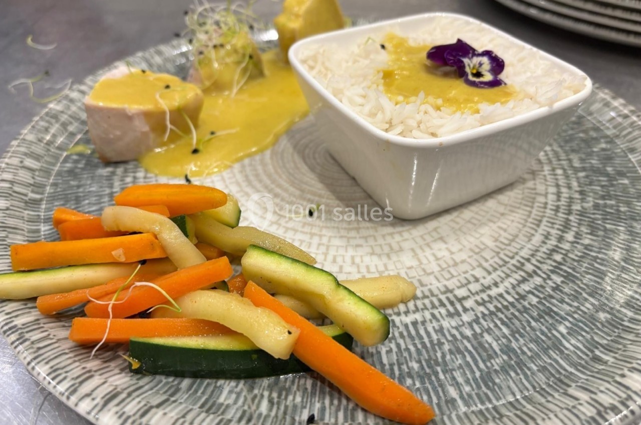 Assiette composée de légumes sautés, riz blanc décoré d'une fleur comestible et poisson nappé de sauce jaune.