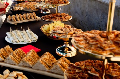 Façade d'un bâtiment en pierre avec une tour, des fenêtres blanches, une terrasse aménagée et un drapeau bleu.