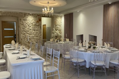 Façade d'un bâtiment en pierre avec une tour, des fenêtres blanches, une terrasse aménagée et un drapeau bleu.