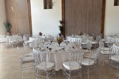Façade d'un bâtiment en pierre avec une tour, des fenêtres blanches, une terrasse aménagée et un drapeau bleu.