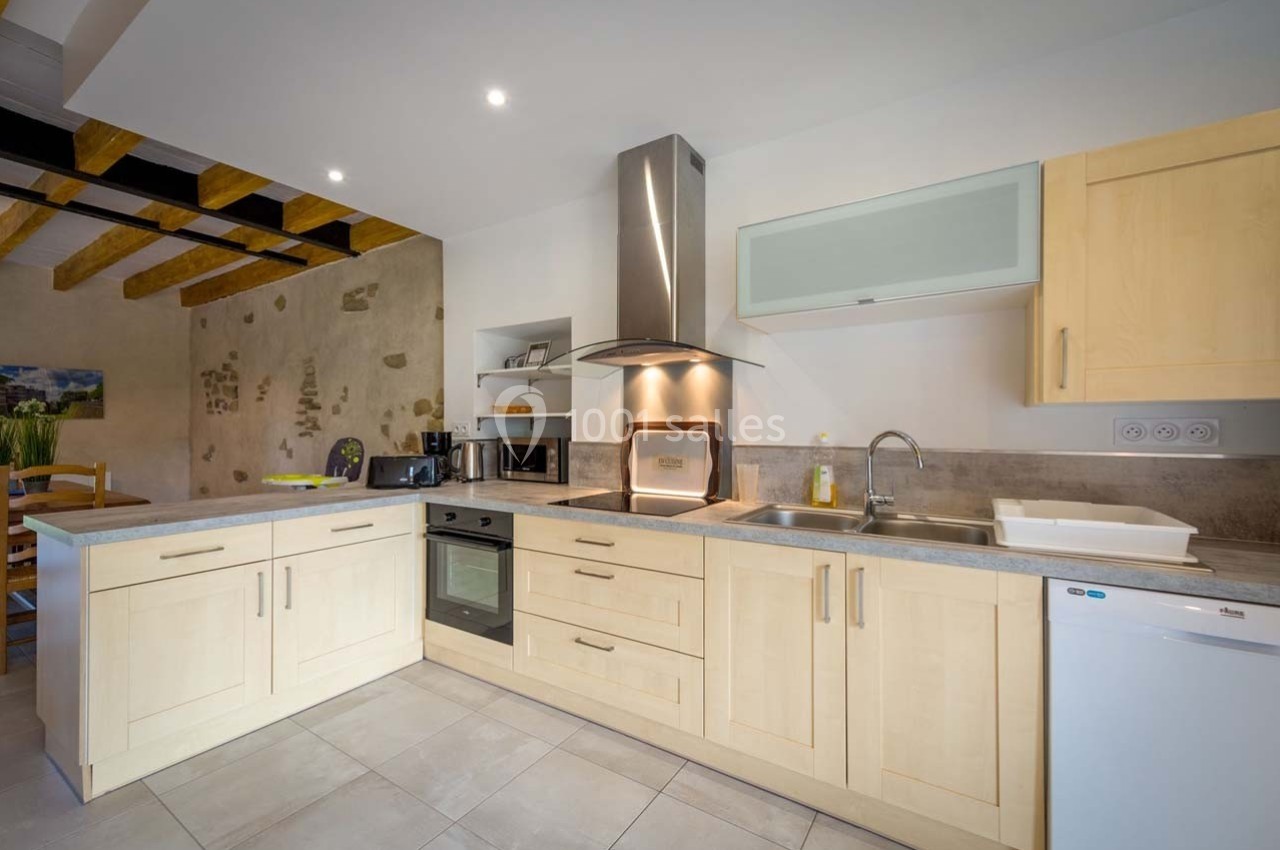 Cuisine moderne avec meubles en bois clair, hotte en inox, évier en inox, et mur en pierre apparente.