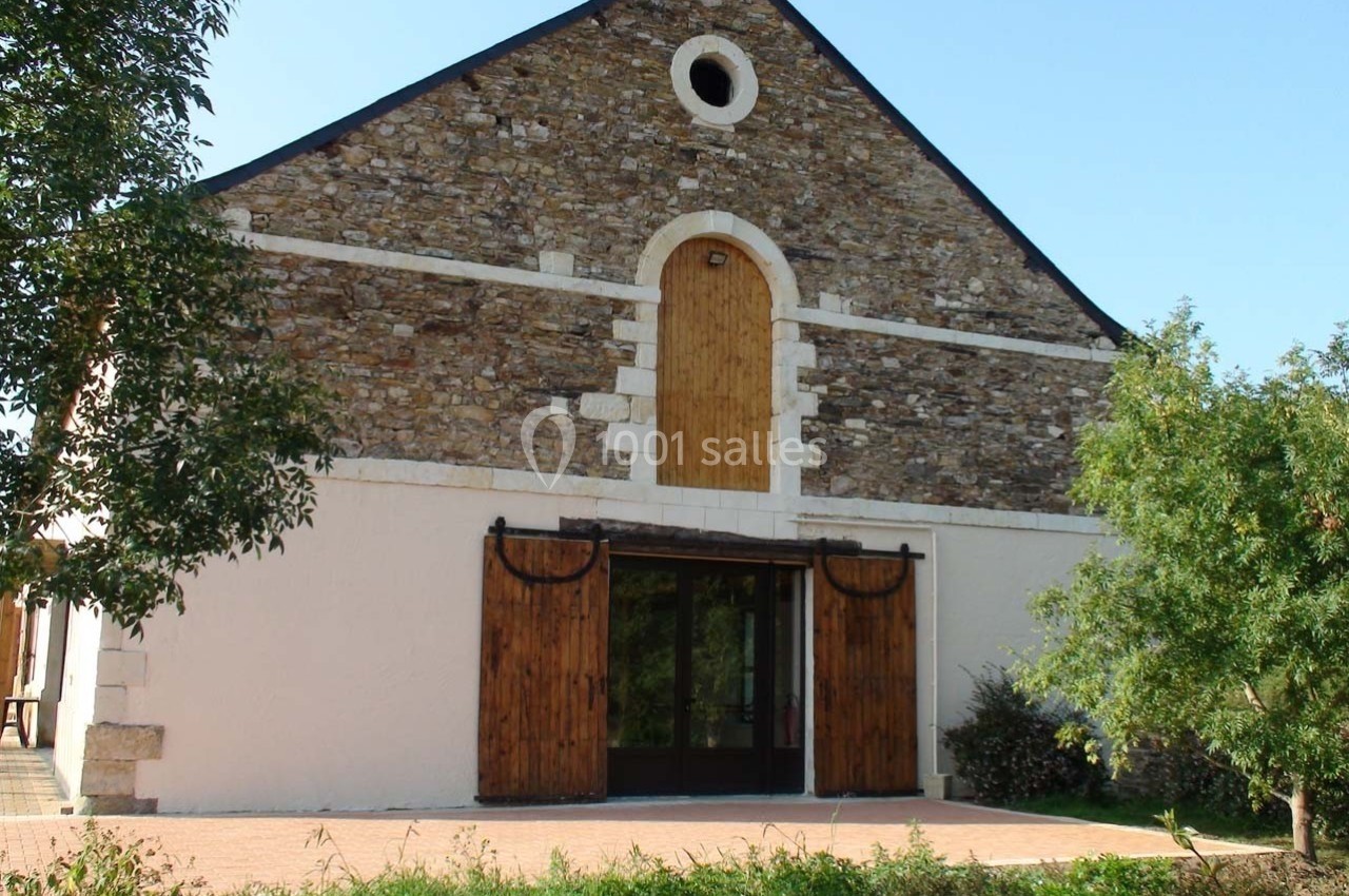 Façade d'un bâtiment en pierre avec une grande porte en bois et des arbres autour.