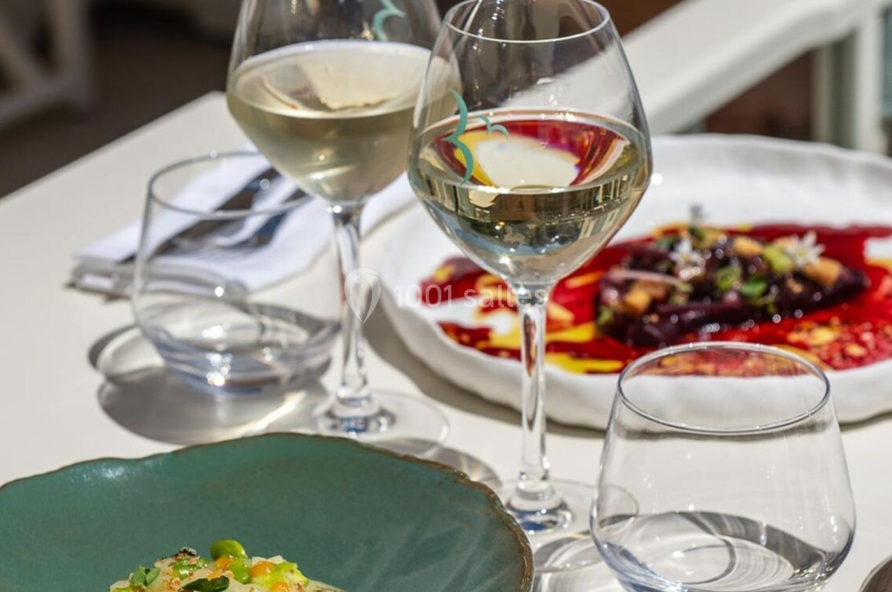 Deux assiettes de plats raffinés et trois verres de vin blanc disposés sur une table extérieure.