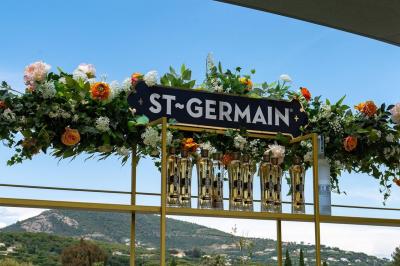 Table rouge avec assiettes, pain, olives, tomates, houmous, boisson orange et lampe, en extérieur.
