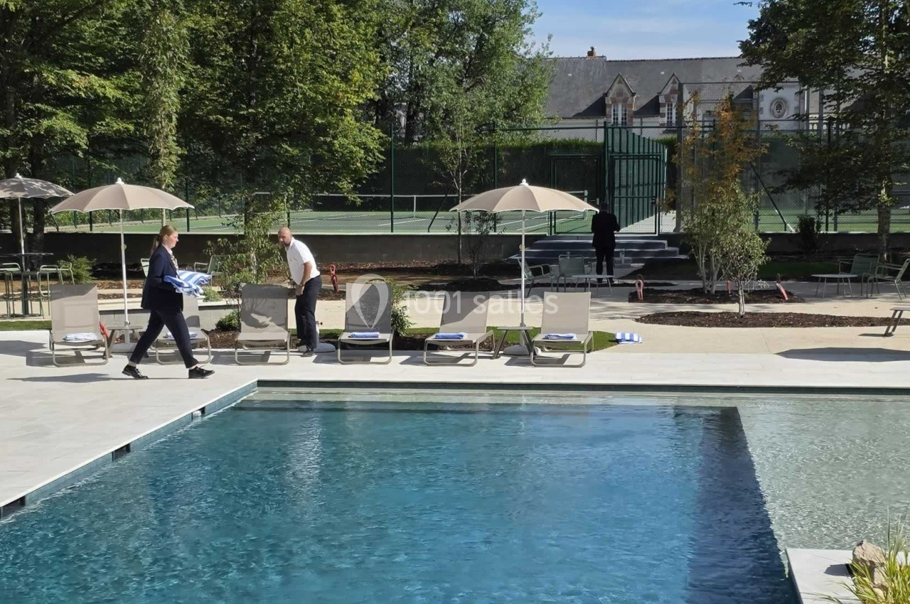 Piscine extérieure avec transats, parasols et terrain de tennis en arrière-plan, entourée de verdure.