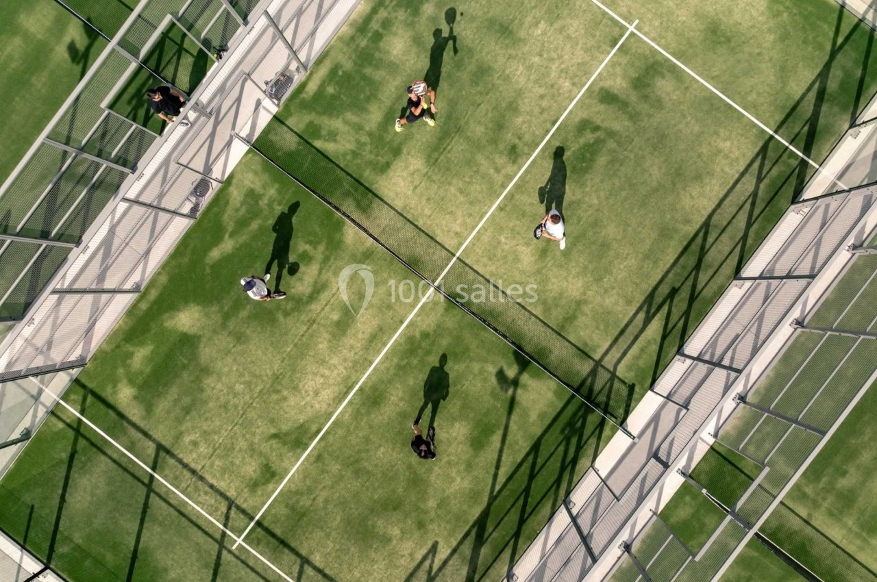 Vue aérienne de quatre personnes jouant au padel sur un terrain entouré de grillages.