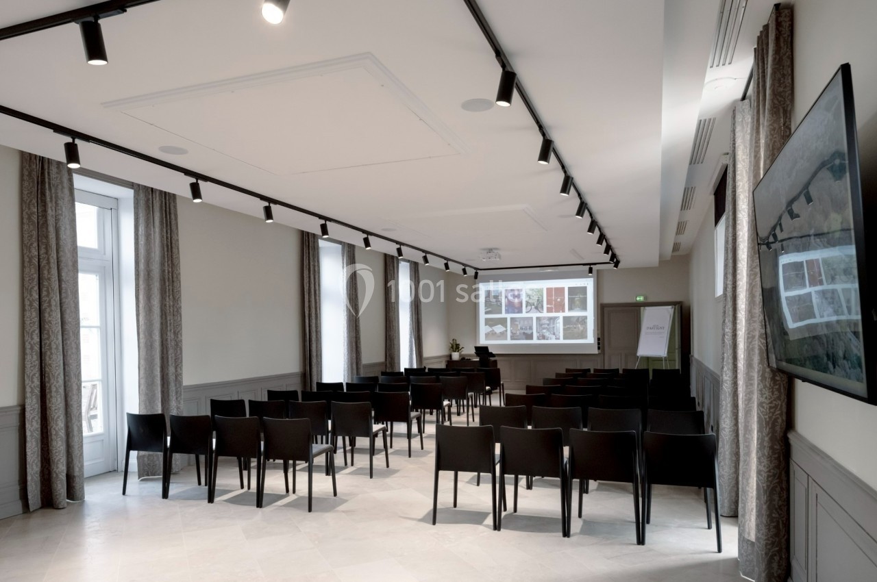 Salle de conférence lumineuse avec des chaises noires alignées, un écran de projection et un tableau de présentation.