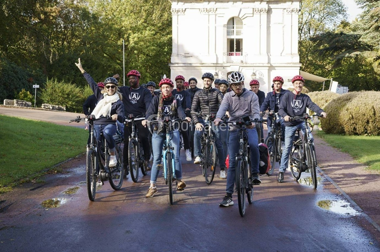 Un groupe de personnes portant des casques rouges posant avec leurs vélos devant un bâtiment blanc dans un parc.