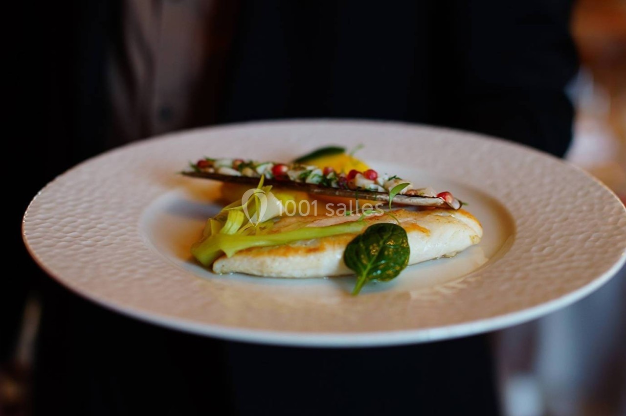 Assiette contenant un filet de poisson, des légumes décoratifs et une garniture colorée, présentée sur une table élégante.