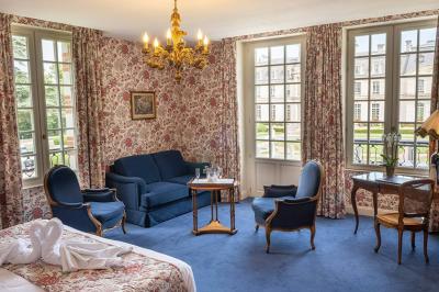 Salle à manger élégante avec table dressée, chaises rouges, murs dorés, lustres et grandes fenêtres avec rideaux jaunes.