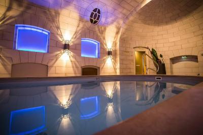 Salle à manger élégante avec table dressée, chaises rouges, murs dorés, lustres et grandes fenêtres avec rideaux jaunes.