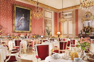 Salle à manger élégante avec table dressée, chaises rouges, murs dorés, lustres et grandes fenêtres avec rideaux jaunes.