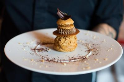 Salle à manger élégante avec table dressée, chaises rouges, murs dorés, lustres et grandes fenêtres avec rideaux jaunes.