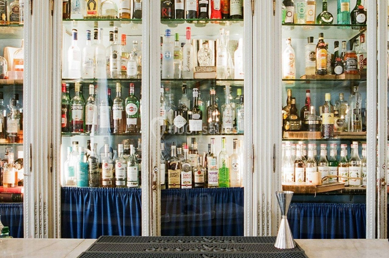 Étagères vitrées remplies de bouteilles d'alcool variées dans un bar, avec un comptoir au premier plan.