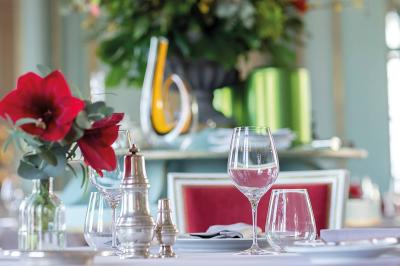 Salle à manger élégante avec table dressée, chaises rouges, murs dorés, lustres et grandes fenêtres avec rideaux jaunes.