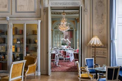 Salle à manger élégante avec table dressée, chaises rouges, murs dorés, lustres et grandes fenêtres avec rideaux jaunes.