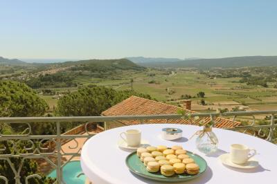 Vue d'une maison en pierre avec piscine, entourée de végétation, donnant sur une vallée et des collines sous un ciel bleu.