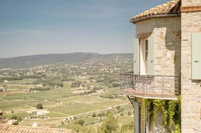 Vue d'une maison en pierre avec piscine, entourée de végétation, donnant sur une vallée et des collines sous un ciel bleu.