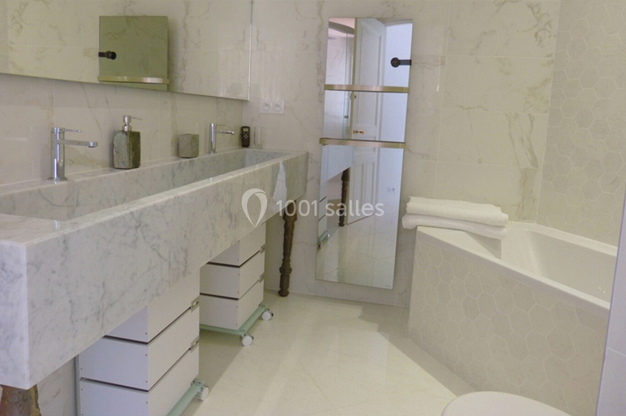 Salle de bain moderne avec lavabo double en marbre, baignoire, miroir et meubles de rangement blancs.