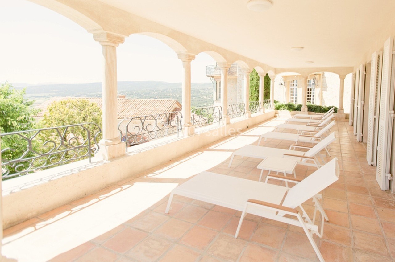 Terrasse lumineuse avec chaises longues blanches, sol en terre cuite et vue dégagée sur la campagne environnante.