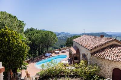 Vue d'une maison en pierre avec piscine, entourée de végétation, donnant sur une vallée et des collines sous un ciel bleu.