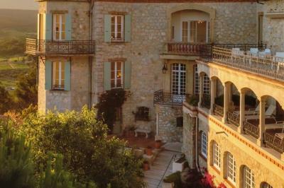 Vue d'une maison en pierre avec piscine, entourée de végétation, donnant sur une vallée et des collines sous un ciel bleu.