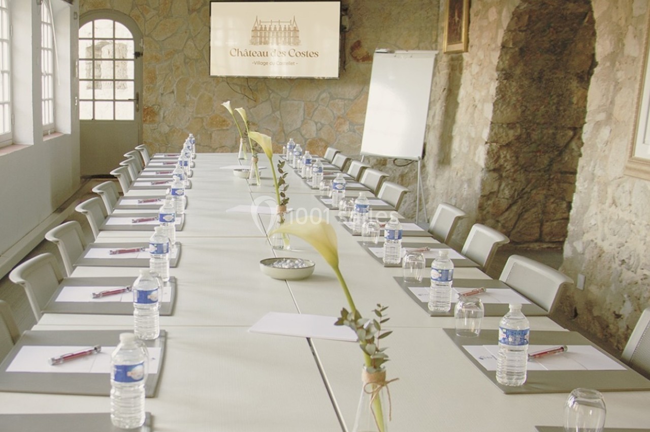 Salle de réunion avec une longue table dressée, équipée de blocs-notes, bouteilles d'eau et fleurs décoratives.