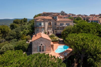 Vue d'une maison en pierre avec piscine, entourée de végétation, donnant sur une vallée et des collines sous un ciel bleu.