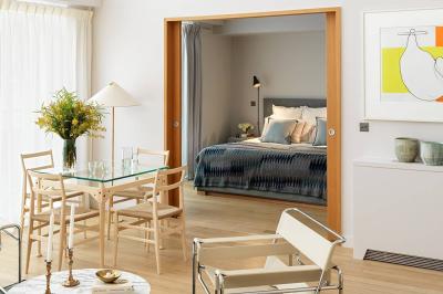 Salon lumineux avec canapé beige, table basse en bois, salle à manger attenante et escalier en arrière-plan.