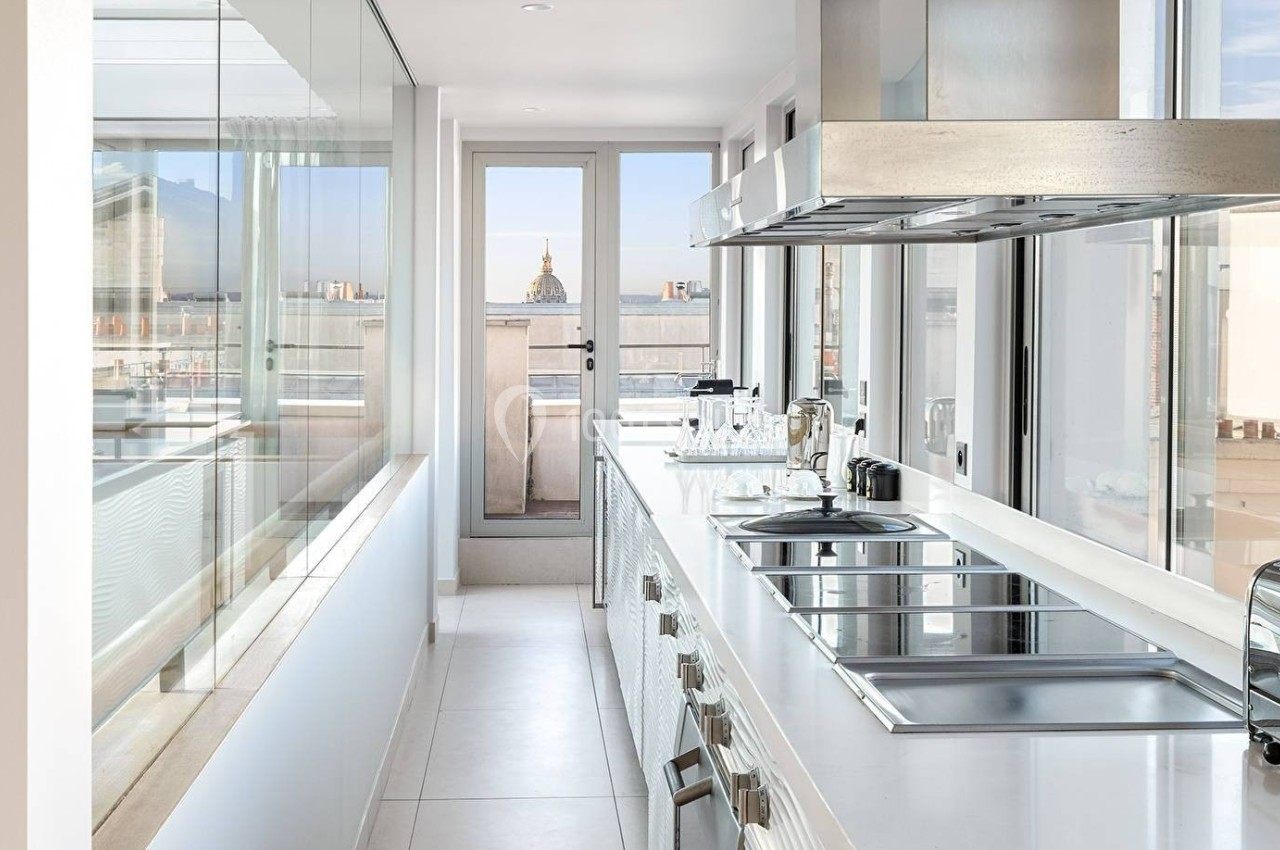 Cuisine moderne lumineuse avec comptoirs blancs, plaques de cuisson, grille-pain et vue sur un bâtiment au dôme doré.