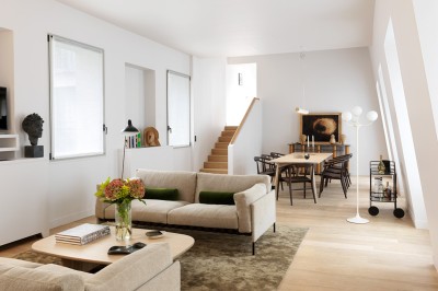 Salon lumineux avec canapé beige, table basse en bois, salle à manger attenante et escalier en arrière-plan.