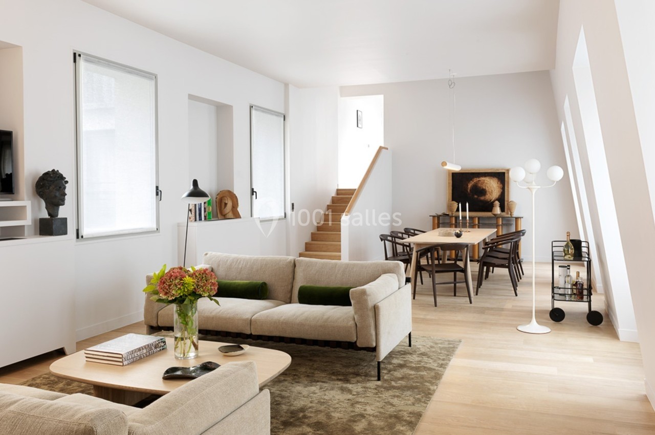 Salon lumineux avec canapé beige, table basse en bois, salle à manger attenante et escalier en arrière-plan.