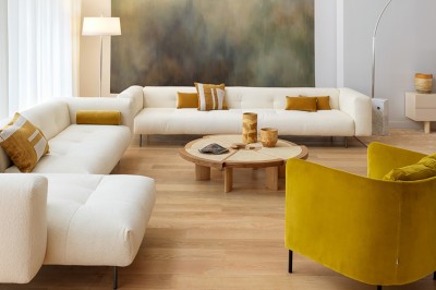 Salon lumineux avec canapé beige, table basse en bois, salle à manger attenante et escalier en arrière-plan.