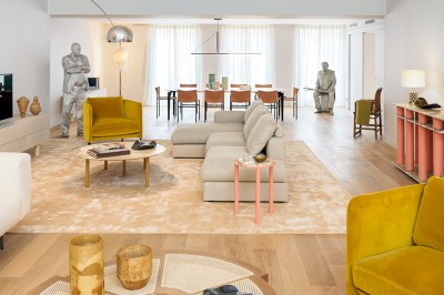 Salon lumineux avec canapé beige, table basse en bois, salle à manger attenante et escalier en arrière-plan.