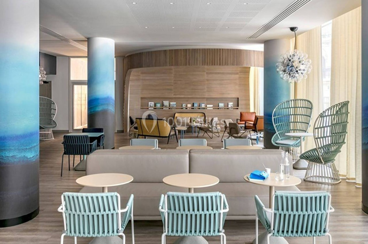 Espace lounge moderne avec mobilier design, fauteuils colorés, tables basses et colonnes décorées de motifs bleus.