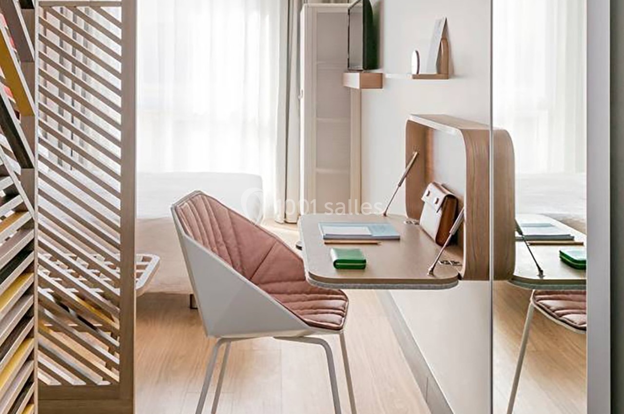 Bureau compact en bois avec chaise rembourrée, installé dans une chambre lumineuse avec lit et étagères en arrière-plan.