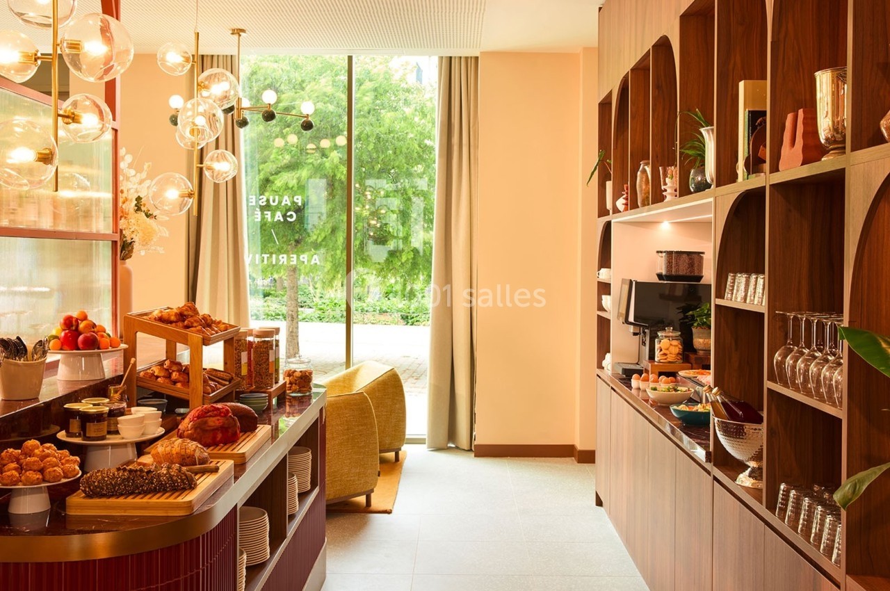 Buffet de petit-déjeuner avec viennoiseries, fruits et boissons, dans un espace lumineux avec vue sur un jardin.