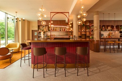 Salle lumineuse avec banquettes en cuir, tables dorées, chaises modernes et coin salon avec fauteuils et canapé.