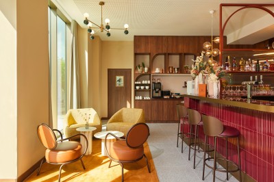 Salle lumineuse avec banquettes en cuir, tables dorées, chaises modernes et coin salon avec fauteuils et canapé.